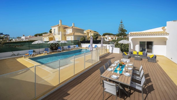 Uma área de piscina no terraço com deck de madeira, cadeiras de espreguiçadeira e uma mesa de jantar para seis pessoas.
