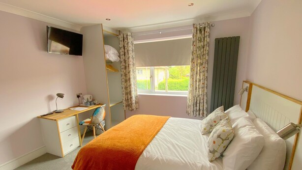 A bedroom with a bed, a desk, a chair, and a television on the wall. - Orchard house bed and breakfast (Swindon)