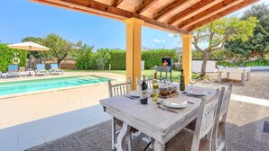 Ein überdachter Essbereich im Freien mit Pool, Grill und gedecktem Tisch.
