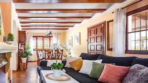 Una sala de estar acogedora con un sofá oscuro, una mesa de centro con una planta en maceta, y un comedor con sillas de madera y una mesa preparada para dos.