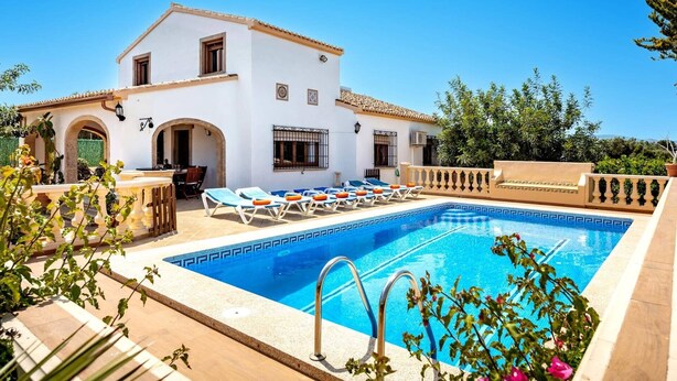Una villa blanca con piscina, zona de estar exterior y vistas al mar.