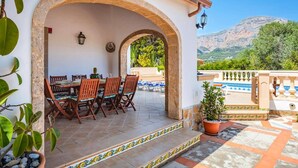 Un área de comedor al aire libre con un arco de piedra, una mesa con sillas y vistas a un paisaje montañoso.