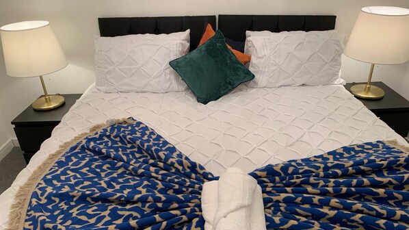 A neatly made bed with a patterned blanket, white pillows, and a teal accent pillow. There are two bedside lamps on black nightstands.