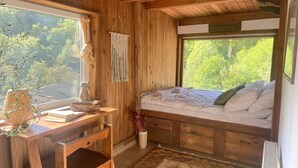 Een slaapkamer in een houten chalet met een bed, een bureau en een raam met uitzicht op groen.