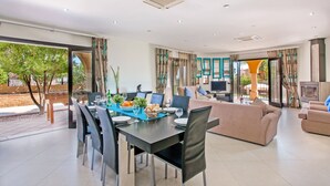 A modern living room with a dining area, large windows, and a TV. - Villa Karlia by Villa Plus (Vale Rebelho)