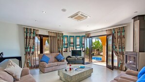 A spacious living room with a beige sofa, a coffee table, and a television. - Villa Karlia by Villa Plus (Vale Rebelho)
