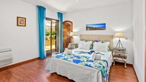 A bedroom with a bed, two bedside tables, a nightstand, a picture on the wall, and a window with curtains. - Villa Karlia by Villa Plus (Vale Rebelho)