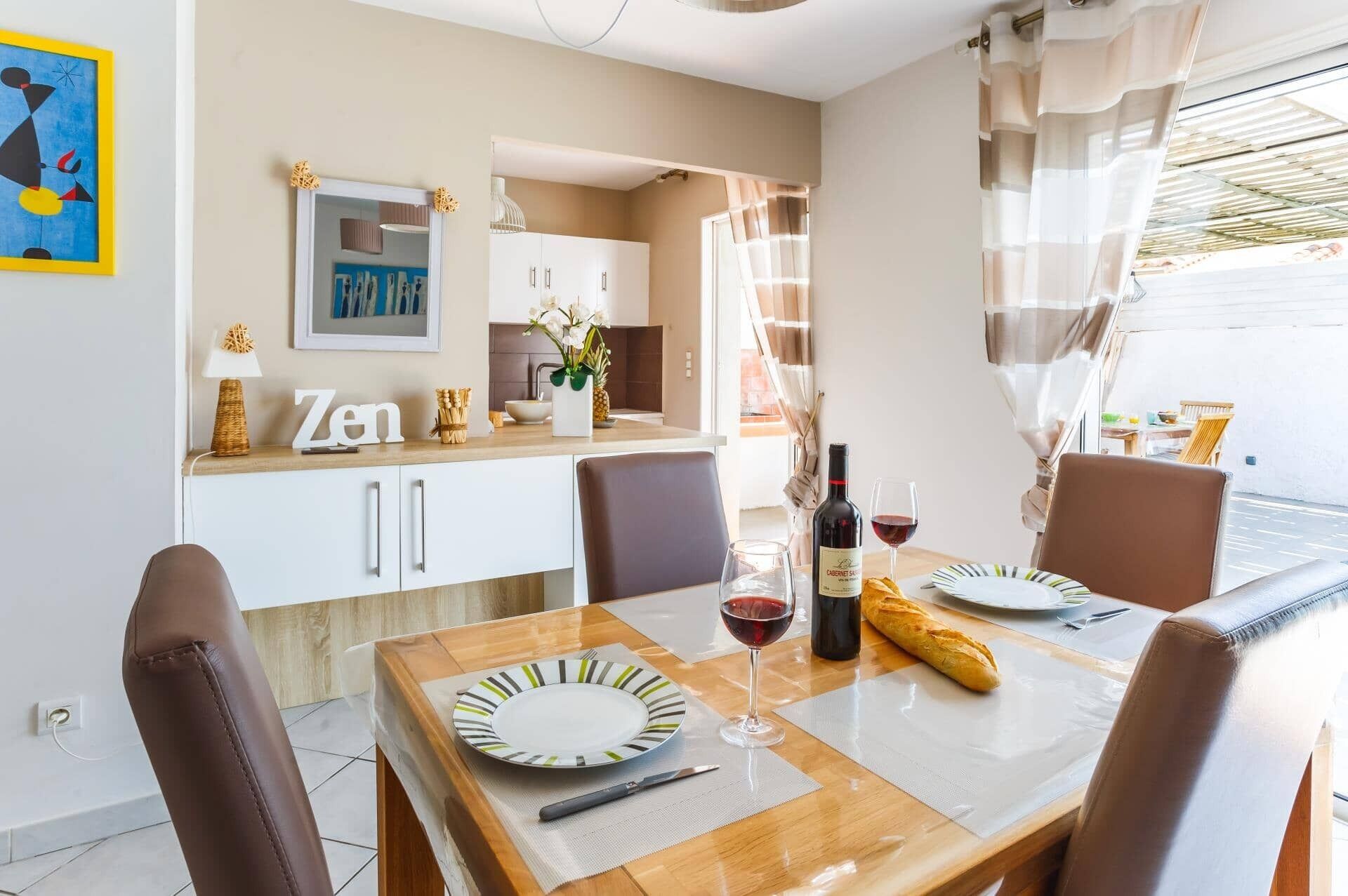 Un coin repas avec une table dressée pour deux personnes, une bouteille de vin et une miche de pain.