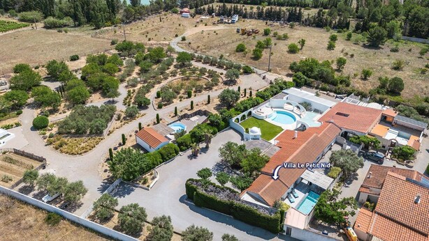 Vue aérienne de la villa Le Petit Nid, avec une piscine, plusieurs bâtiments et des espaces paysagers environnants.
