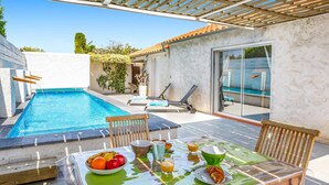 Un espace aménagé au bord de la piscine, avec une table préparée pour le petit-déjeuner, une piscine et des chaises longues.