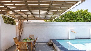 Un espace extérieur abrité comprenant une piscine, des meubles en bois et un mur blanc.
