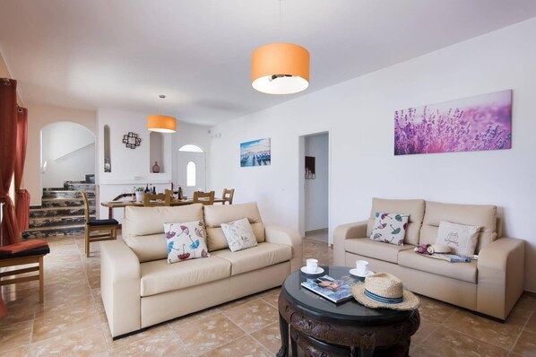 A spacious living room with two beige sofas, a coffee table, and a dining area with a table and chairs.