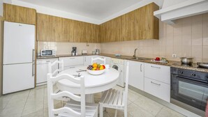 A modern kitchen with white cabinetry, a central island with seating, and a built-in oven. - Villa Luis Gale by Villa Plus (Vale Rebelho)