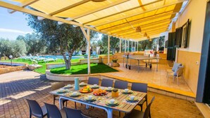 An outdoor dining area with a covered patio, a table set for four, and a view of a pool and garden in the background. - Villa Maria Rosaria by Villa Plus (Ceglie Messapica)