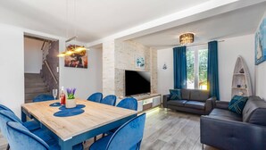 A modern living room with a wooden dining table, blue chairs, a grey sofa, and a TV on a stone wall. - Villa Melani Vita by Villa Plus (Marčana)