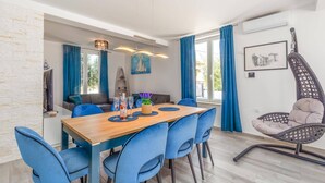 A dining area with a wooden table and blue chairs, a hanging chair, and a painting on the wall. - Villa Melani Vita by Villa Plus (Marčana)
