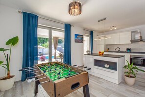 Une cuisine moderne avec des meubles blancs, une table de baby-foot et une vue sur l’extérieur.