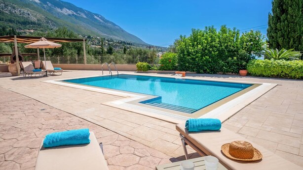 Ein rechteckiger Pool mit klarem, blauem Wasser, umgeben von Liegestühlen und einer Pergola.