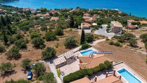 Eine Vogelperspektive auf ein Küstendorf mit Häusern, einem Swimmingpool und Blick aufs Meer.