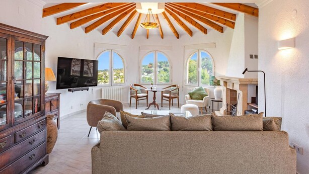 A spacious living area with a high ceiling, a fireplace, a dining table with chairs, and a television mounted on the wall. - Villa Murales by Villa Plus (El Tosalet)