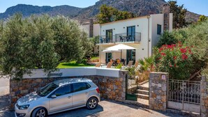 A modern two-story house with a stone facade, a balcony with outdoor furniture, and a car parked in the driveway. - Villa Nefeli Green by Villa Plus (Chersonisos)