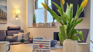 Ett vardagsrum med en soffa, ett soffbord, en välkomstskylt och en krukväxt.