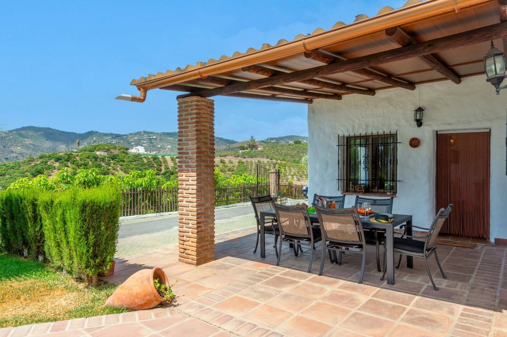 A patio with a table and chairs, a brick pillar, and a view of a hilly landscape.