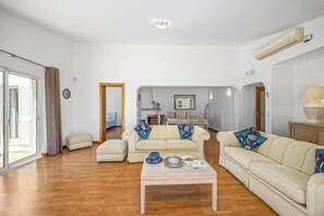 A spacious living room with a wooden floor, two cream-colored sofas, a coffee table, and a dining area in the background. - Villa Pinehill by Villa Plus (Praia do Carvoeiro)