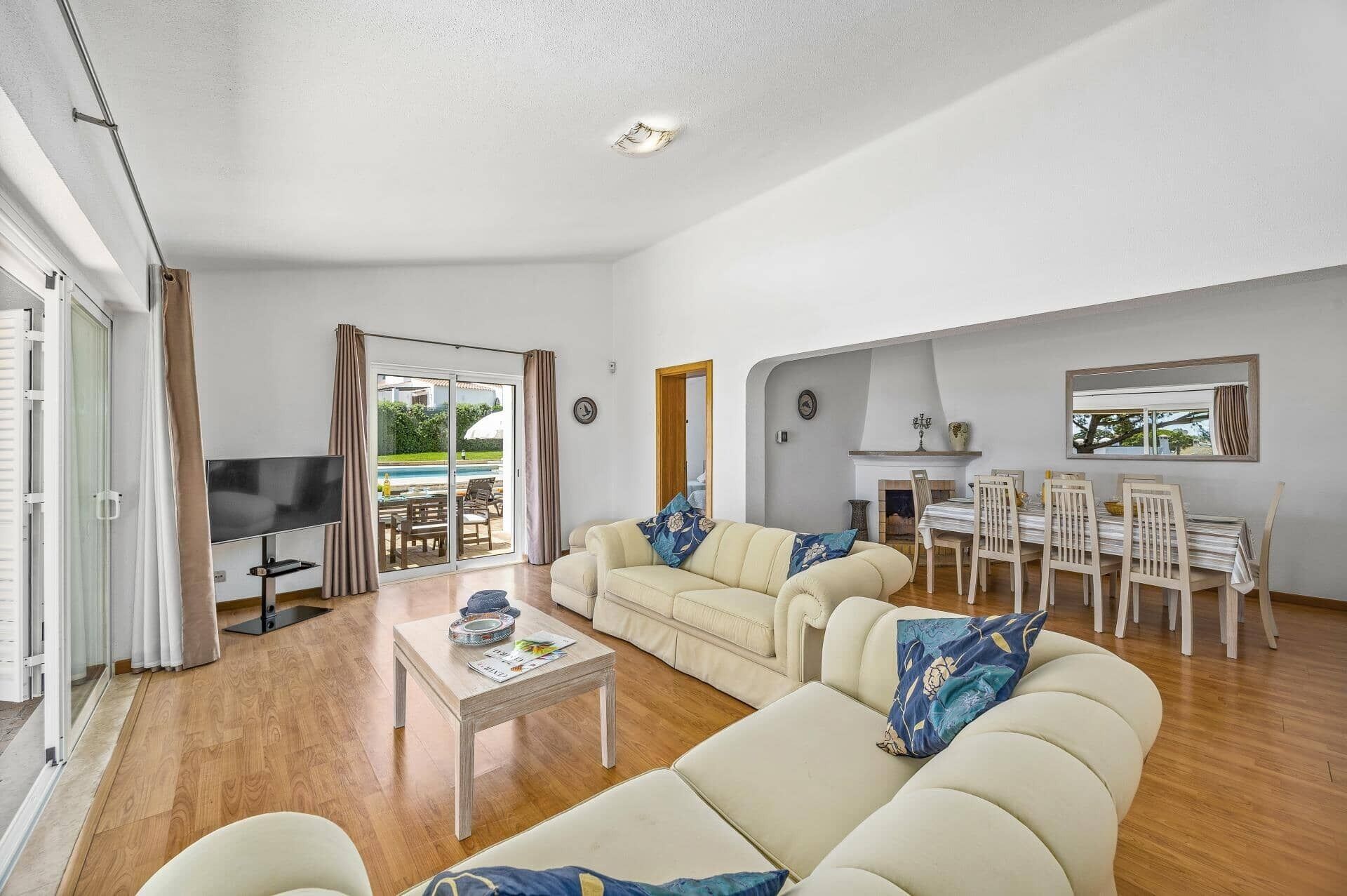 A spacious living room with a sofa set, a dining table with chairs, a TV, and a sliding glass door leading to a balcony.