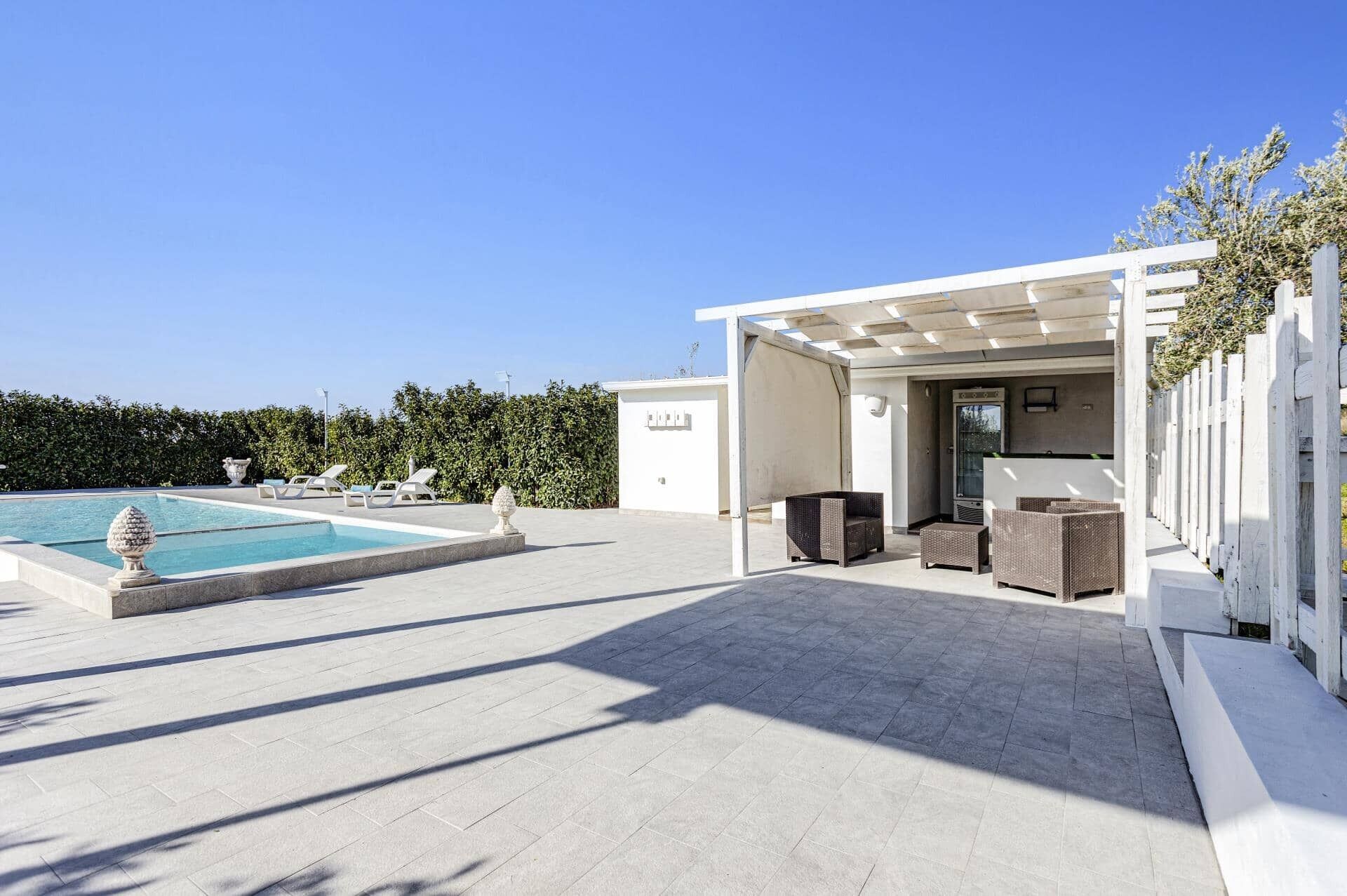Zona junto a la piscina con piscina, sillas de descanso y un área de estar cubierta.