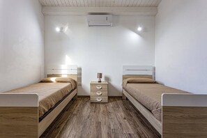 Ein Zimmer mit zwei Betten, einem kleinen Nachttisch mit Schubladen, einer Wandklimaanlage und Holzboden.