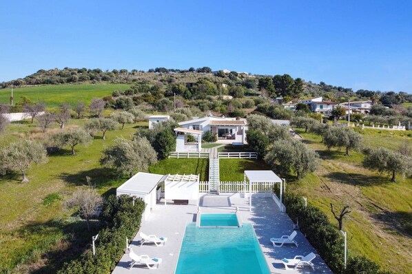 Eine moderne Villa mit Pool, umgeben von Olivenbäumen und einer hügeligen Landschaft.