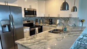 A modern kitchen with a stainless steel refrigerator, a built-in microwave, a gas stove, and a sink with a glass backsplash. - Relax in your one bedroom Oceanfront Suite in Tavernier FL. Florida Keys. (Tavernier)