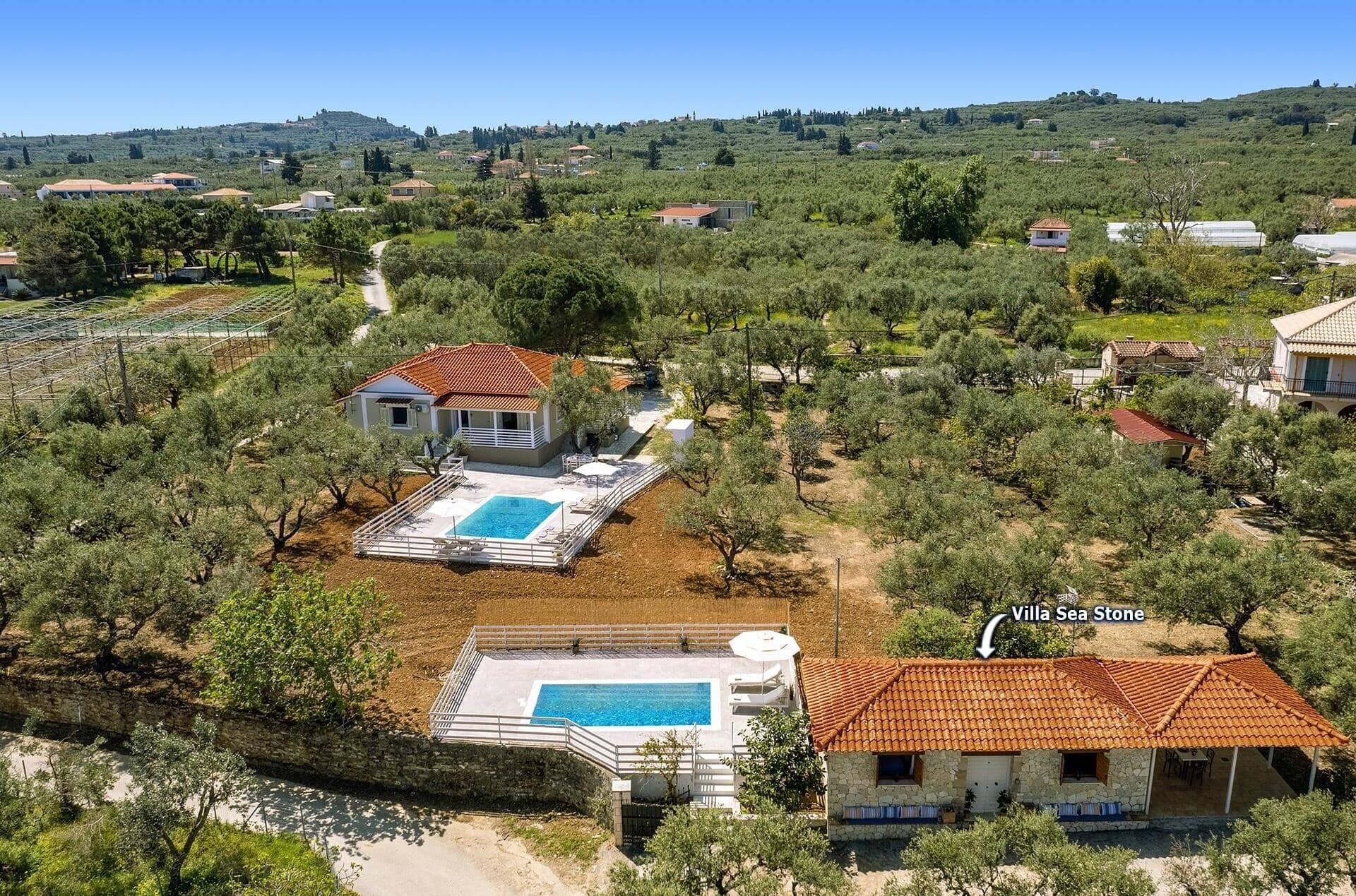 Una vila amb piscina, envoltada d'oliveres i un paisatge amb turons.