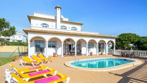 En hvid villa med pool, gule liggestole og en overdækket terrasse.