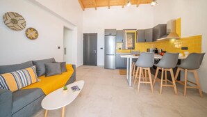 A modern living room with a sofa, a coffee table, and a kitchen area with a refrigerator, stove, and bar stools.