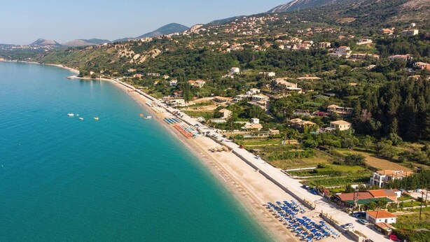 An aerial view of a coastal town with a beach lined with blue umbrellas and a clear blue sea.