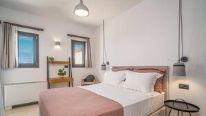 A modern bedroom with a bed, bedside tables, a small desk, and a hanging light fixture.
