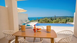 A terrace with a wooden table, white wicker chairs, a small table with bottles, and a view of the sea.