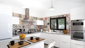 A modern kitchen with white cabinets, a stainless steel range hood, a window with a view, and a built-in oven. - Villa Taiga by Villa Plus (Playa Blanca)