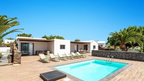 A modern pool area with lounge chairs, a swimming pool, and a stone wall. - Villa Taiga by Villa Plus (Playa Blanca)