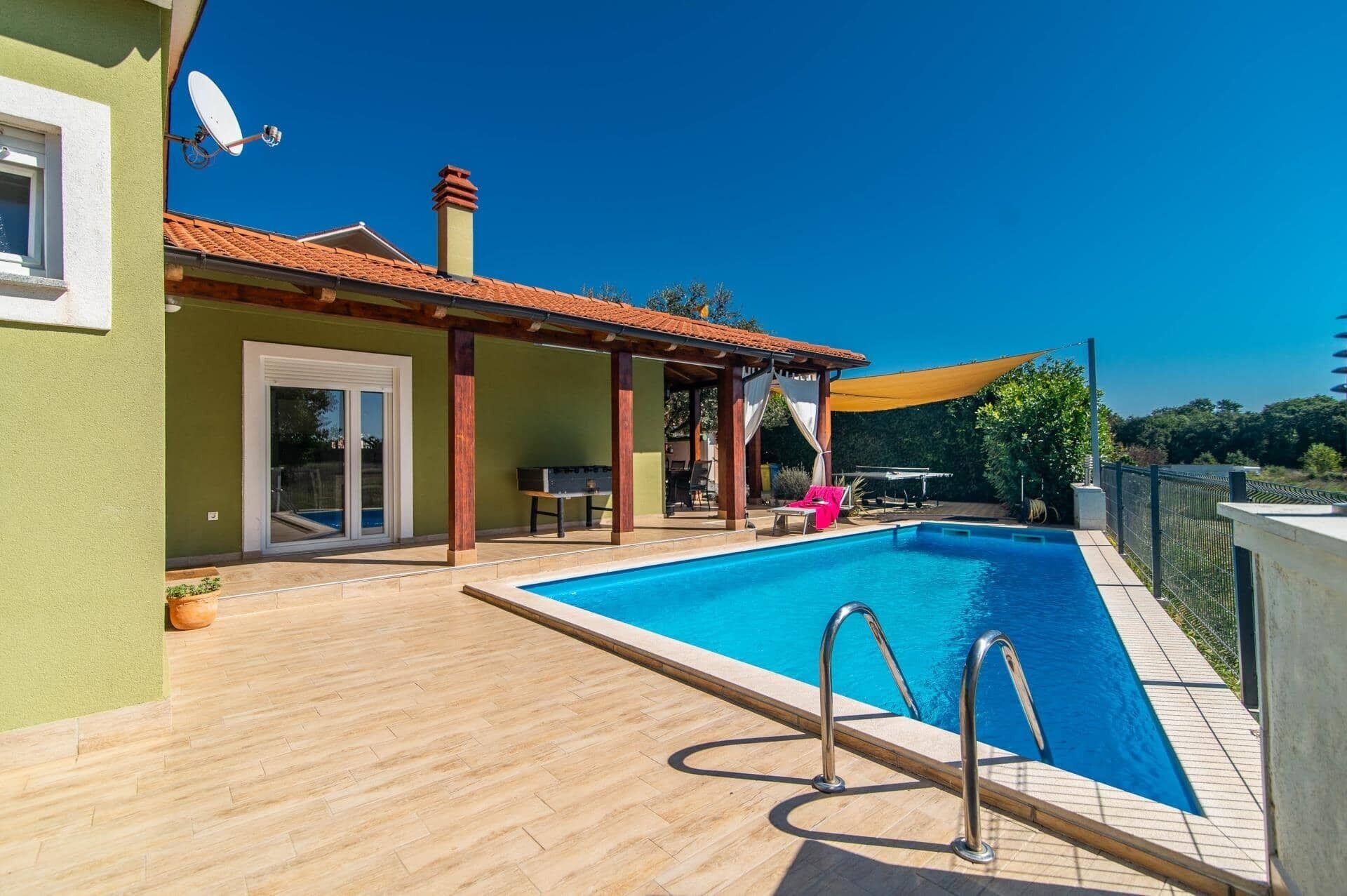 A swimming pool with a wooden deck, a covered seating area, and a satellite dish on the building.