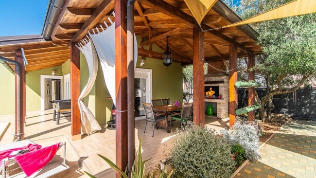 Une terrasse extérieure couverte, avec une table et des chaises, un hamac rouge et un espace barbecue.