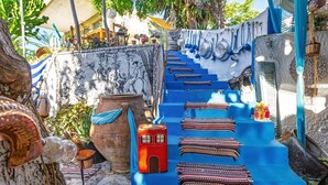 A staircase with colorful woven rugs, a red stool, and hanging kitchen utensils.