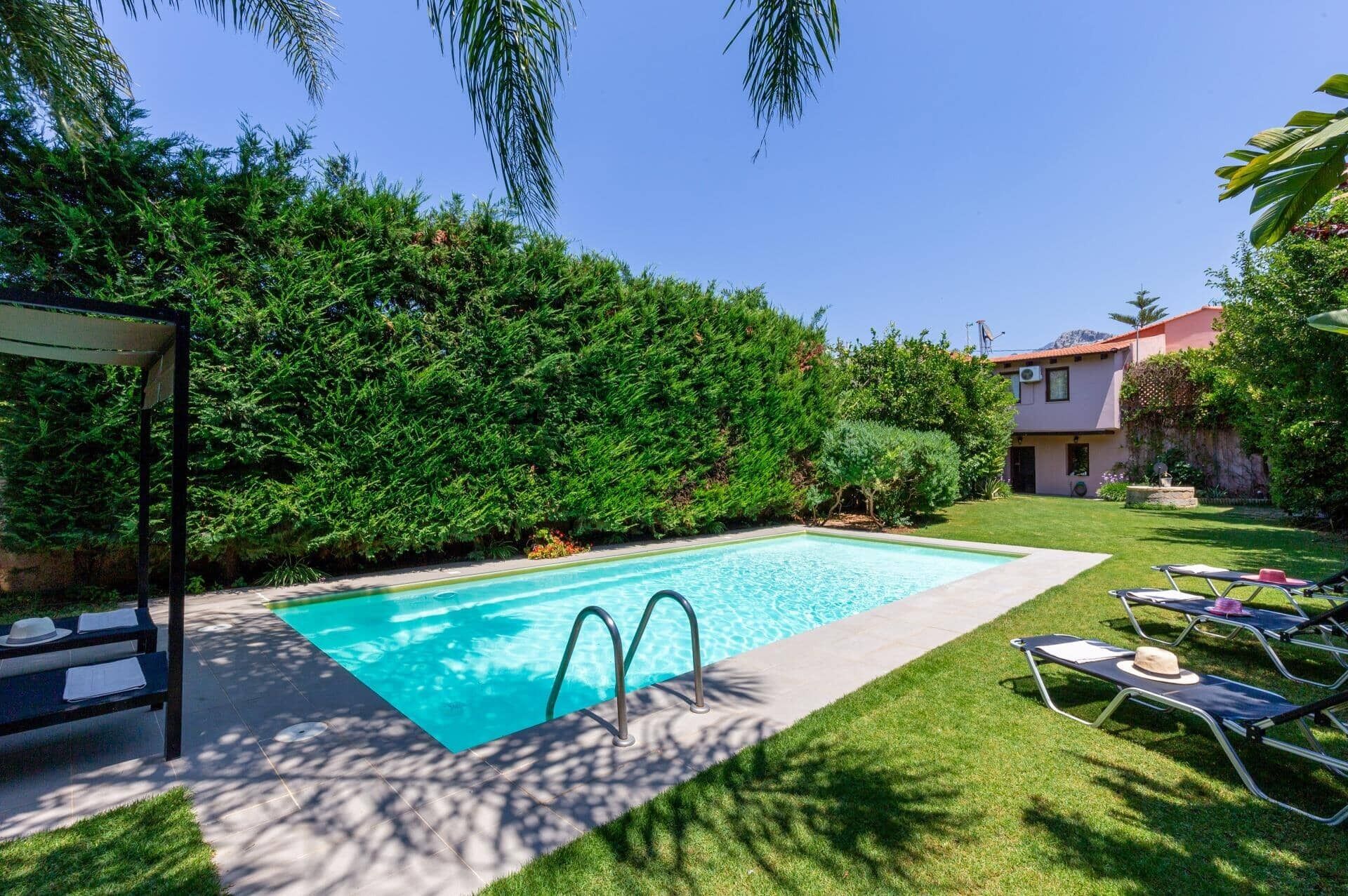 A swimming pool with a clear blue water, surrounded by lush greenery and a well-maintained lawn.