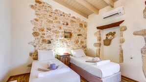 A room with two beds, a stone wall, an air conditioning unit, and a wooden ceiling.