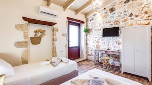 A room with a stone wall, a wooden ceiling, a sofa, a television, and a wardrobe.