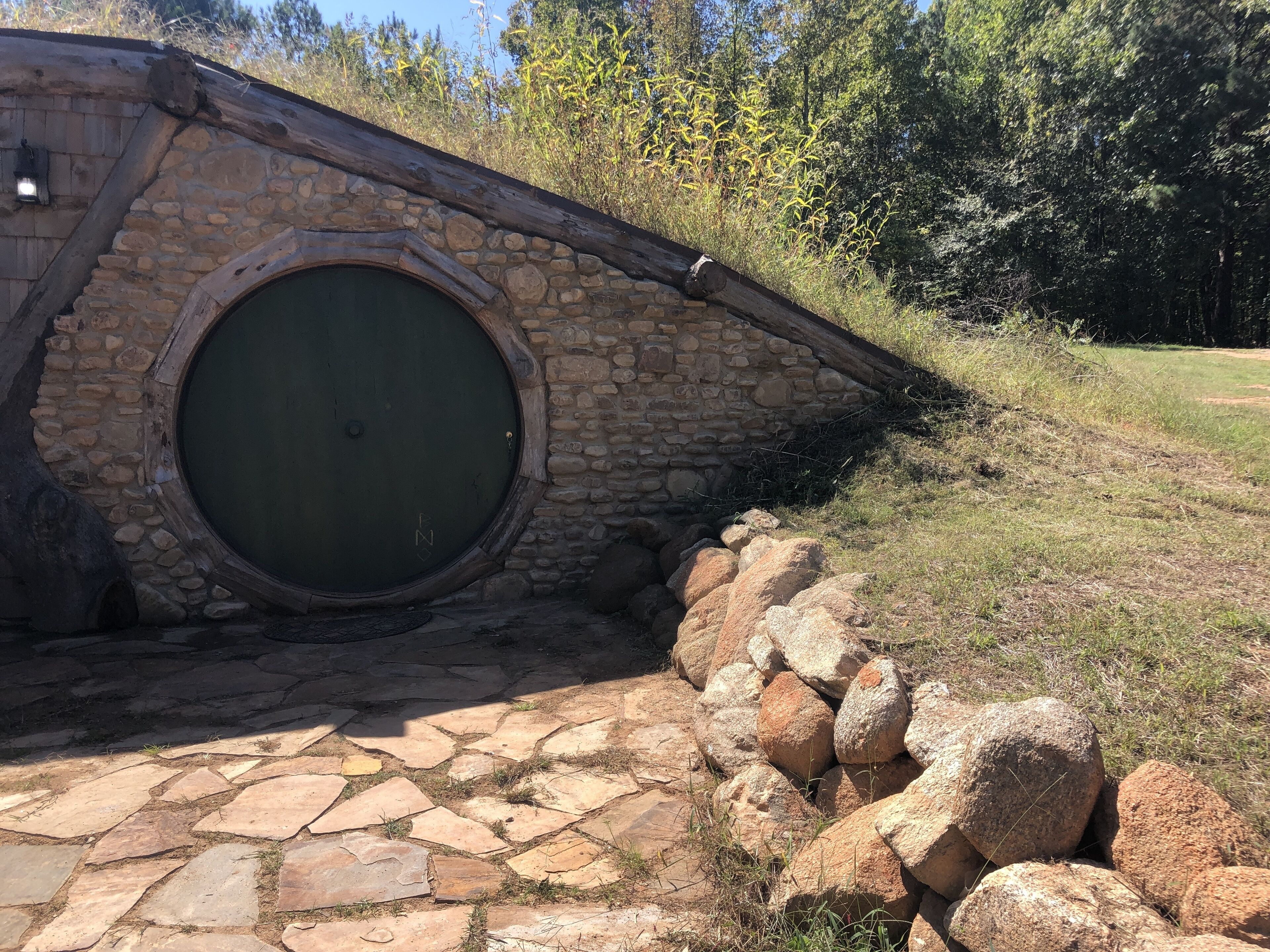 Una estructura de piedra con un arco de entrada circular, rodeada por un muro de piedra y un acceso empedrado.