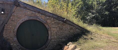 Una estructura de piedra con un arco de entrada circular, rodeada por un muro de piedra y un acceso empedrado.