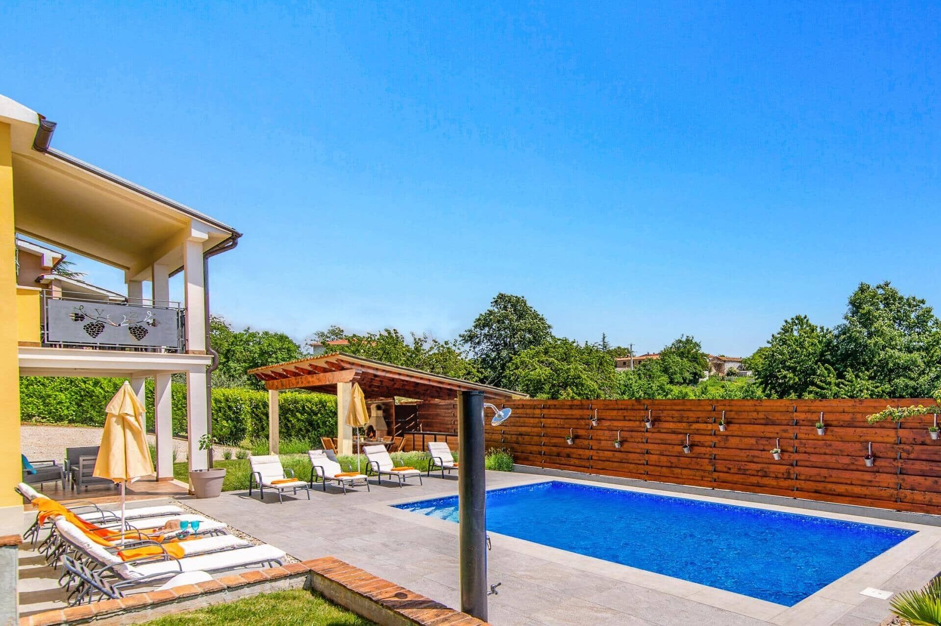 Un espace piscine aménagé avec des chaises longues, une pergola et une clôture en bois.